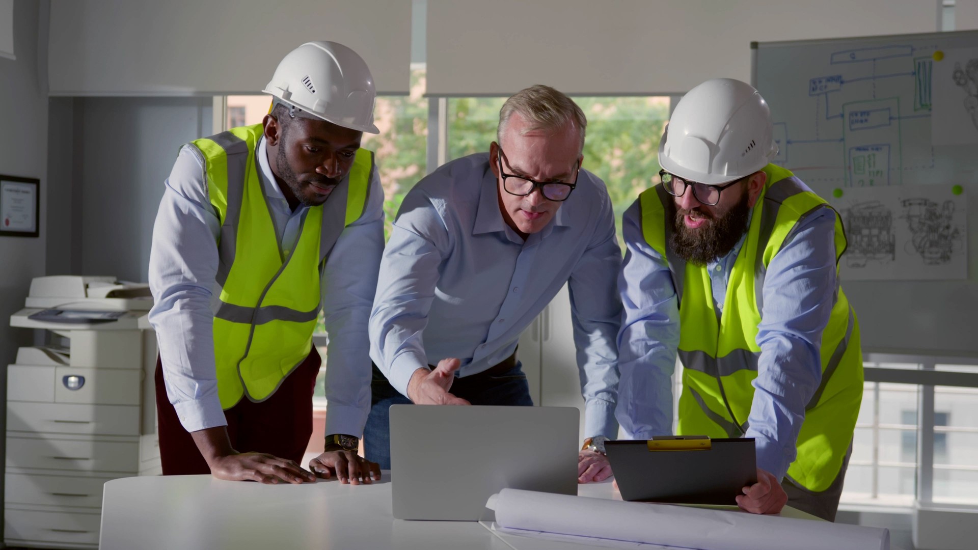 Engineers and contractor brainstorm in office with laptop and clipboard
