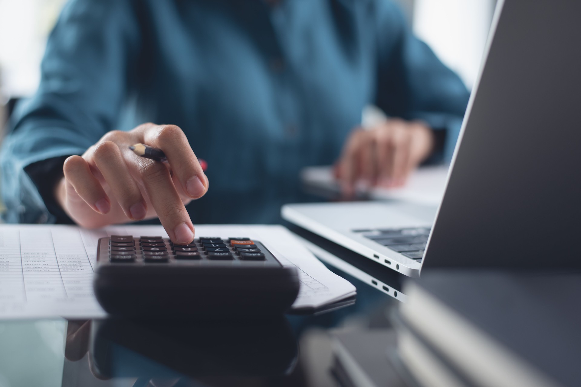 Close up of businesswoman or accountant working on calculator to calculate business data, accountancy document, financial report and laptop computer on office table, business analysis, budget management concept